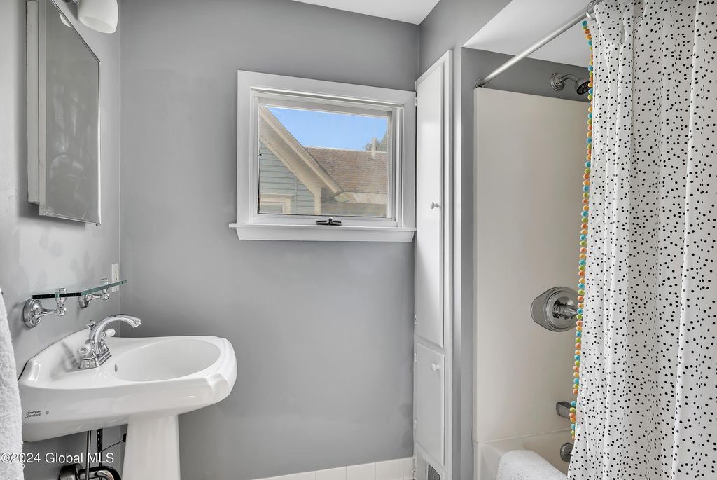 A bathroom with a sink , toilet , shower and window.