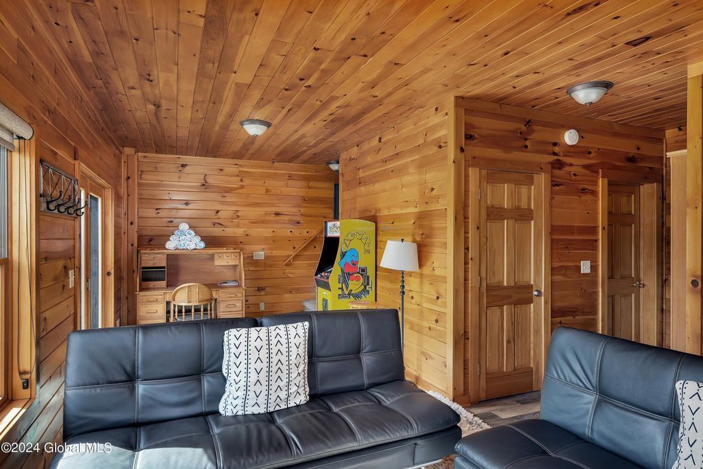 A living room in a log cabin with a black couch and a wooden ceiling.