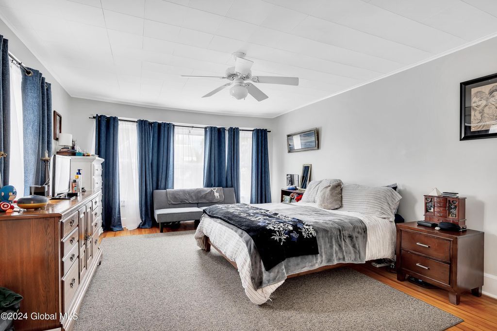 A large bedroom with a bed , dresser , couch and ceiling fan.