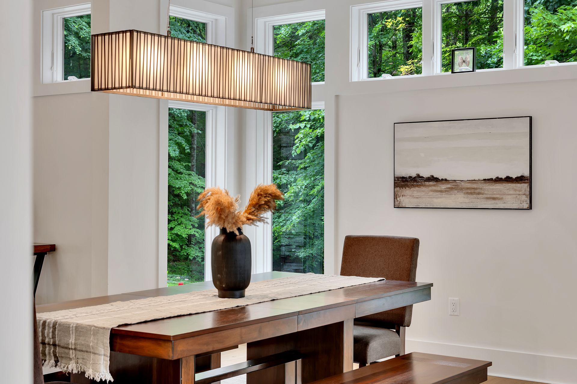 A dining room table with a vase of dried flowers on it.