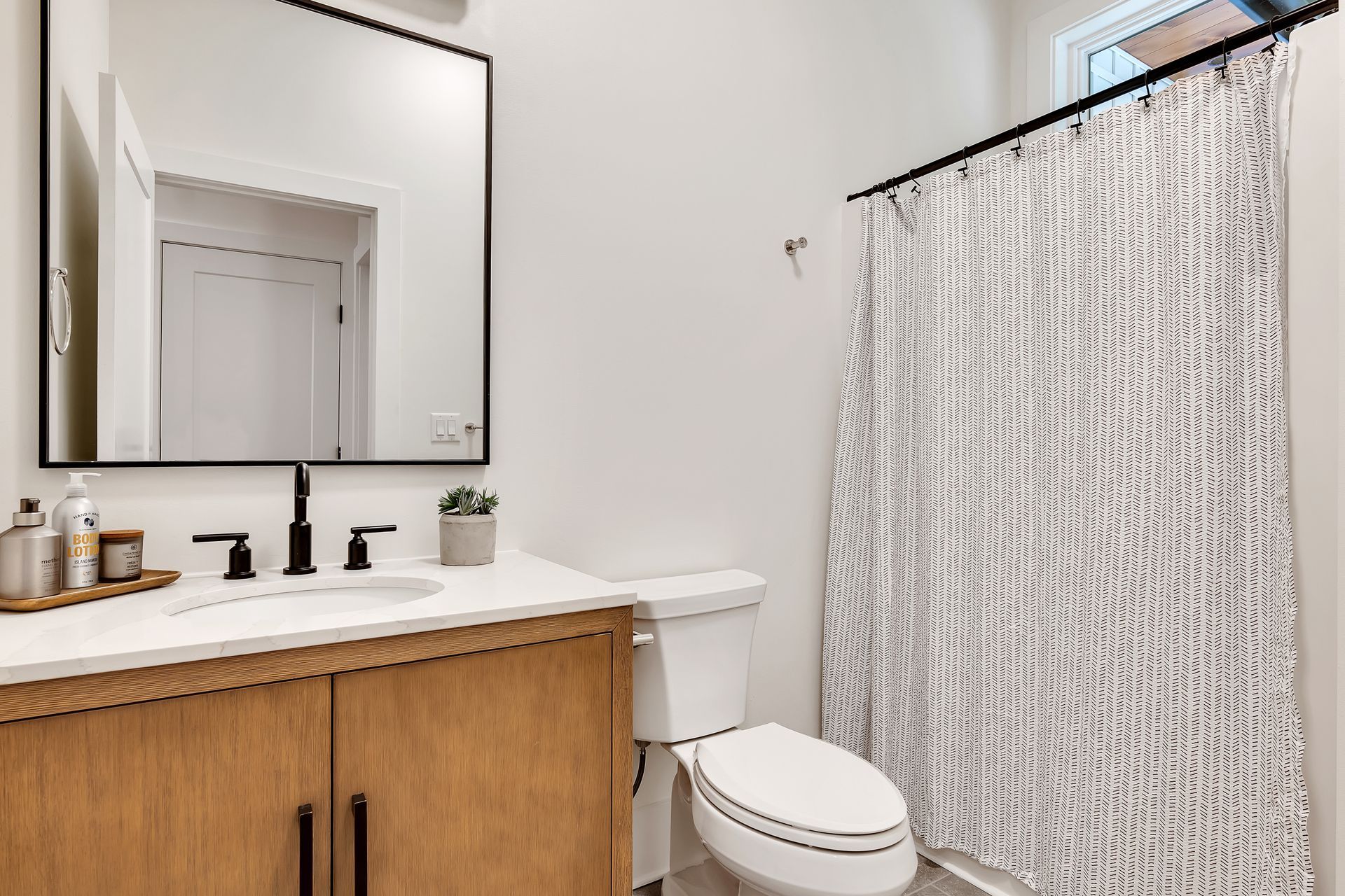 A bathroom with a toilet , sink , mirror and shower curtain.