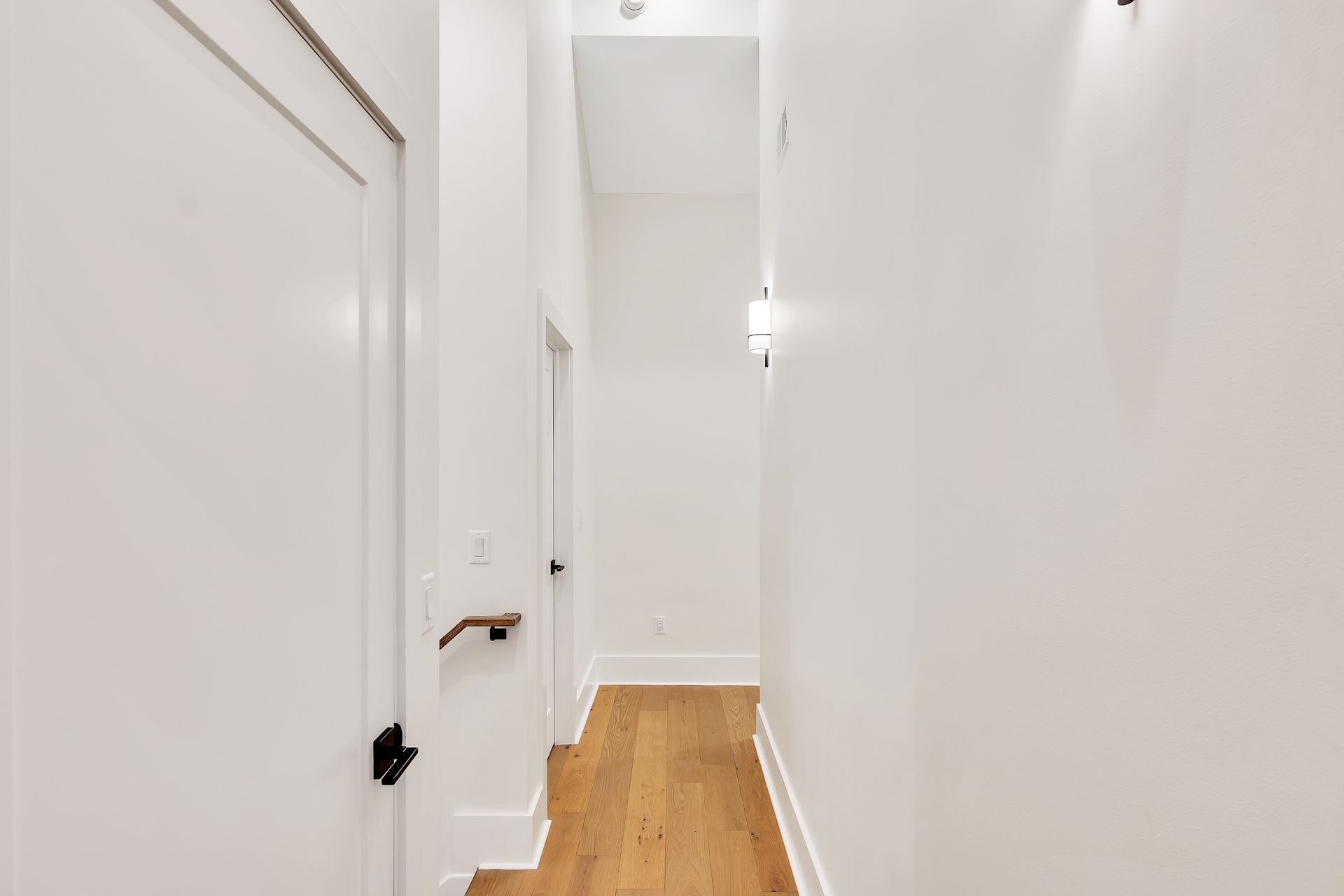 A long hallway with white walls and wooden floors in a house.