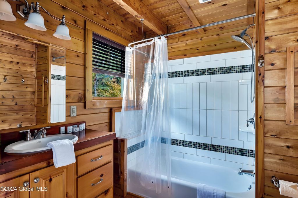 A bathroom in a log cabin with a tub , sink , mirror and shower curtain.