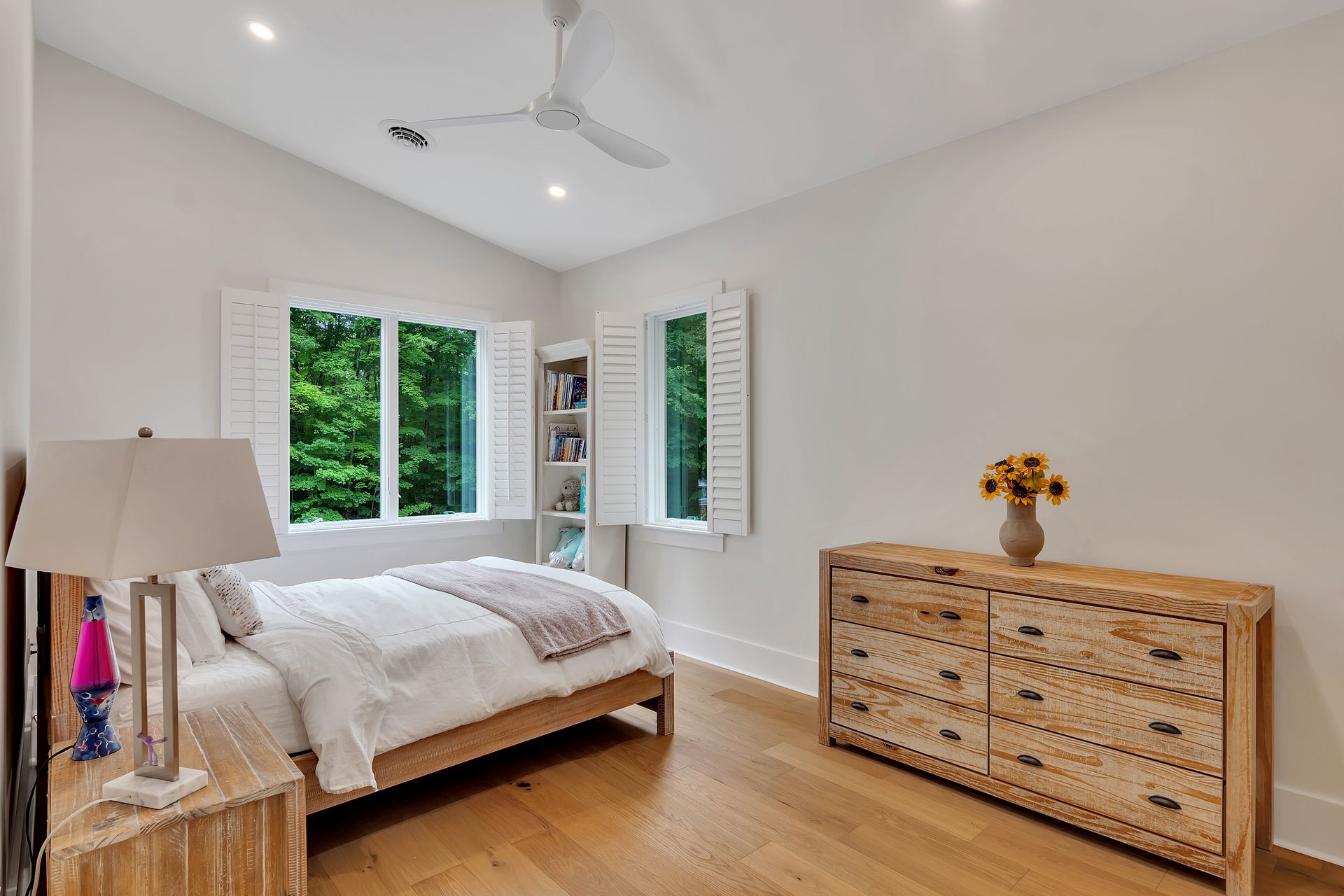 A bedroom with a bed , dresser , lamp and ceiling fan.