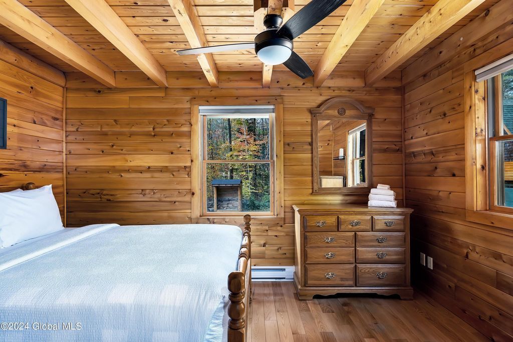 A bedroom in a log cabin with a bed , dresser , mirror and ceiling fan.