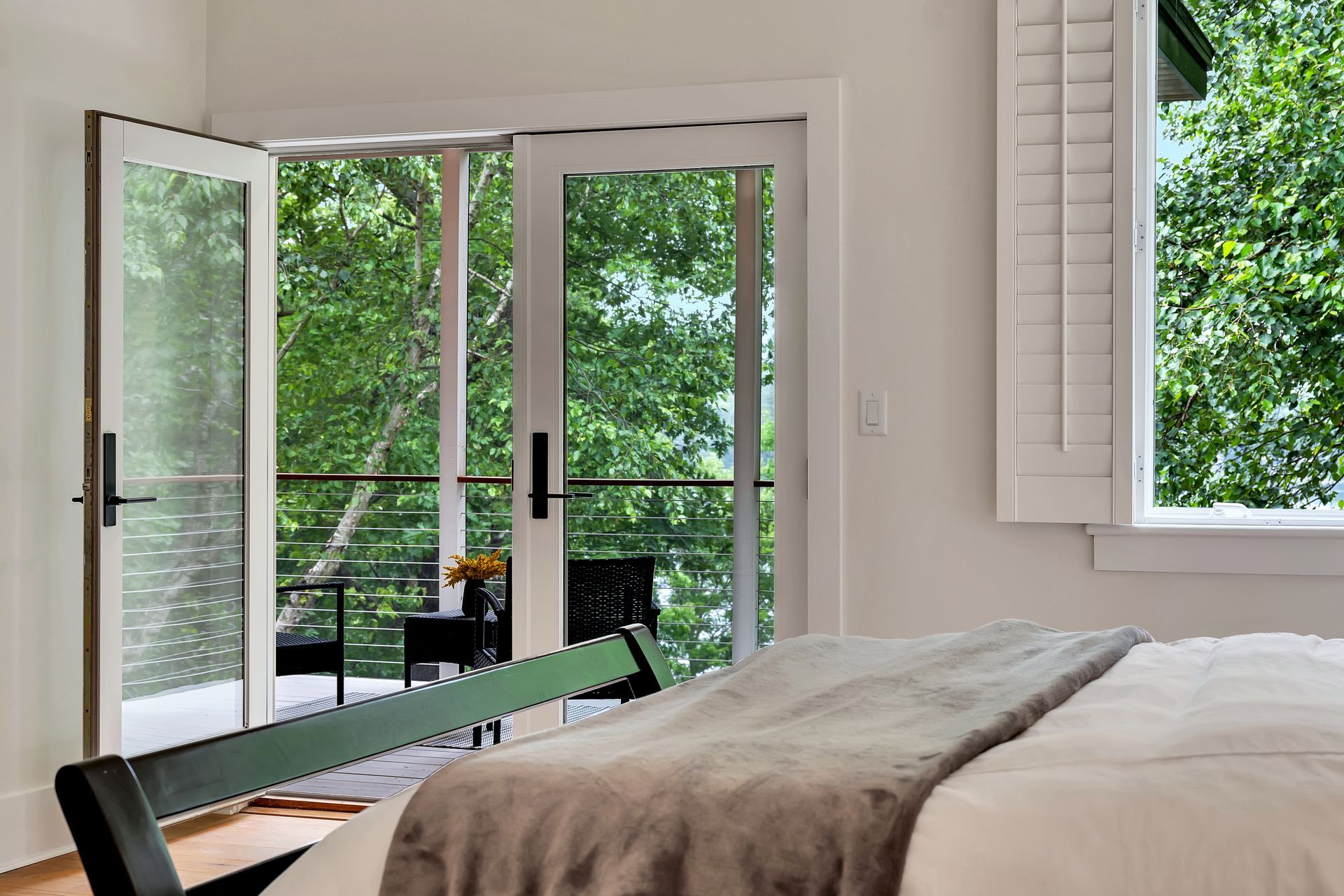 A bedroom with a bed and a balcony with a view of trees.