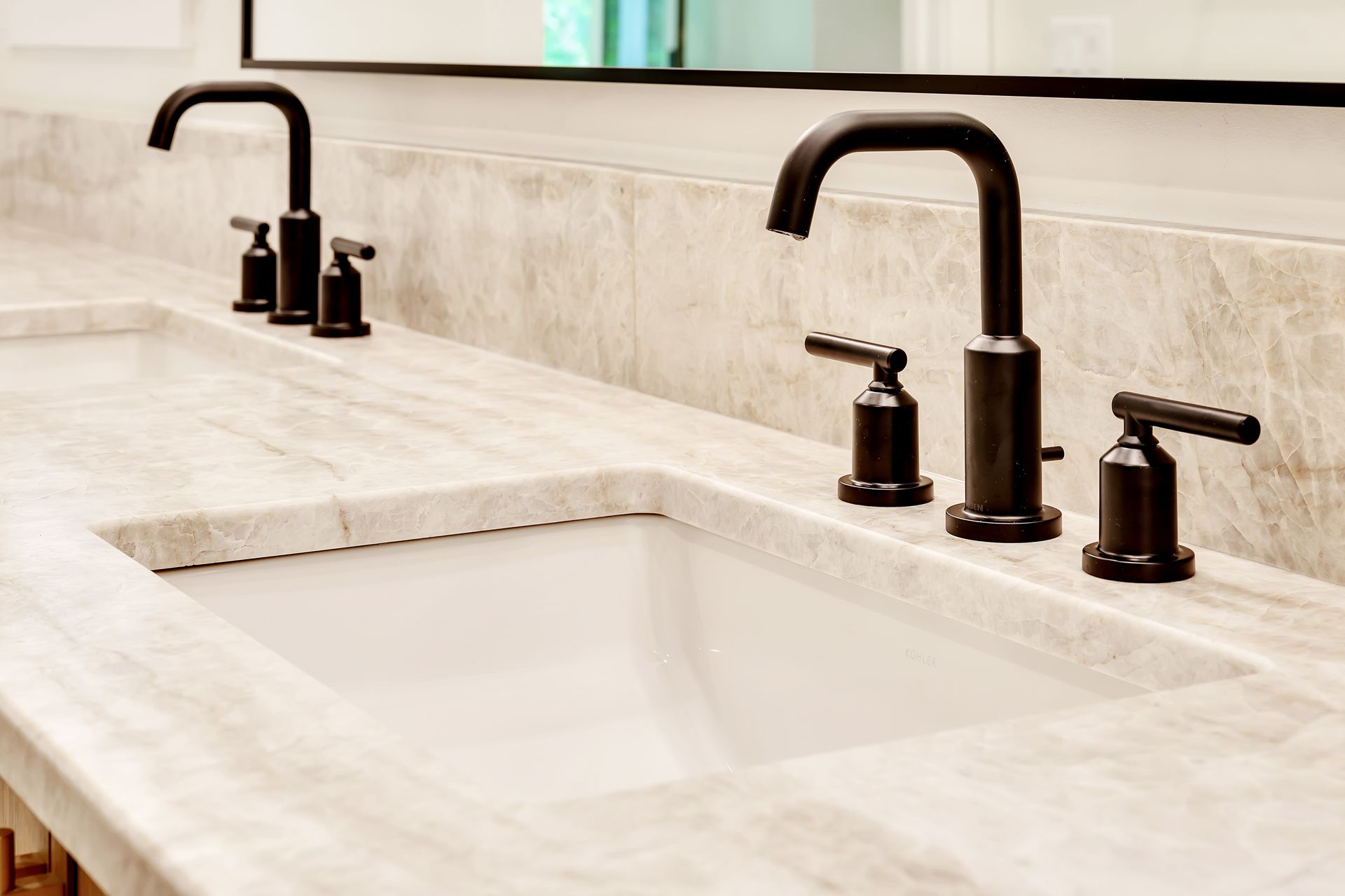 A bathroom sink with two black faucets and a mirror.