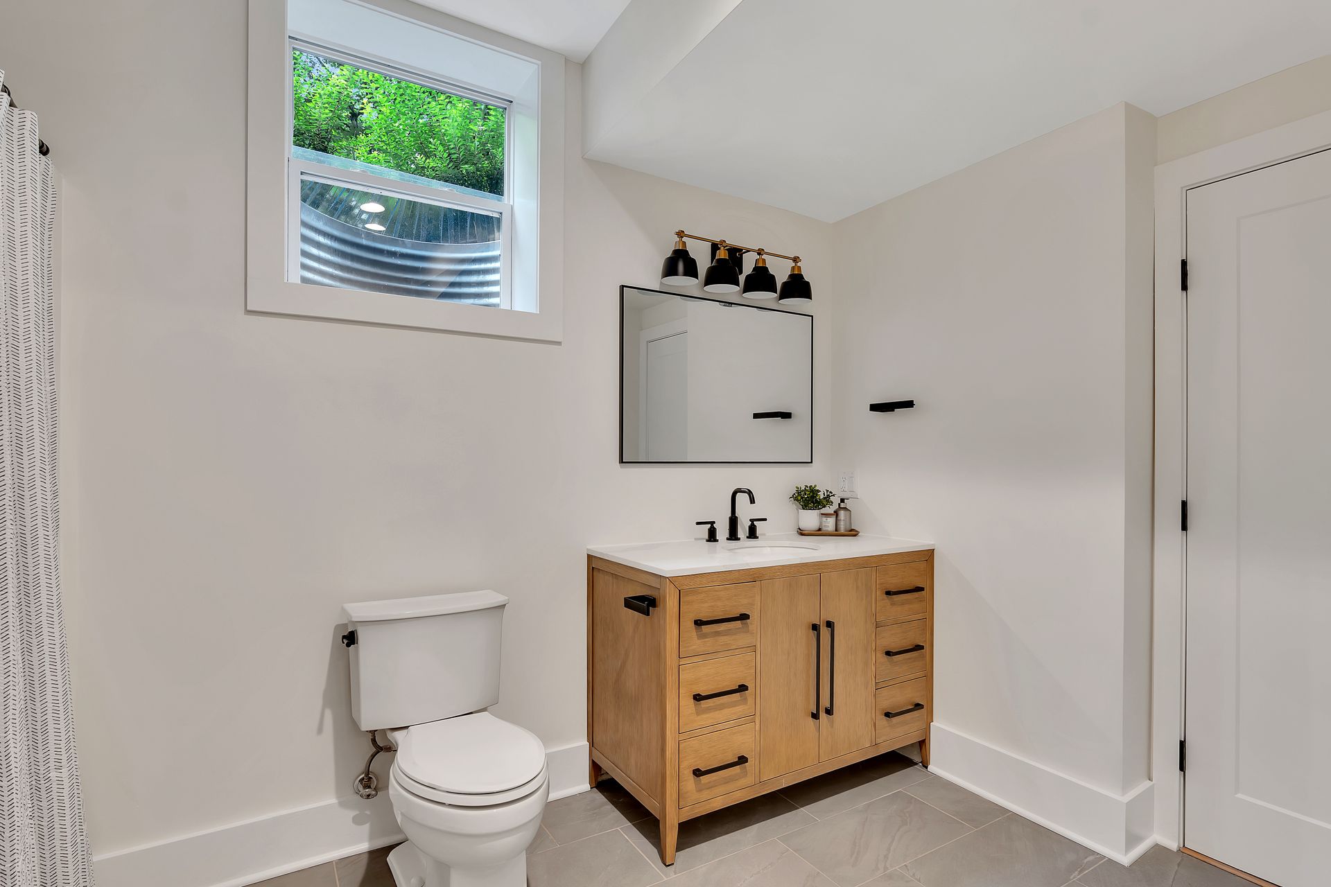A bathroom with a toilet , sink , mirror and window.