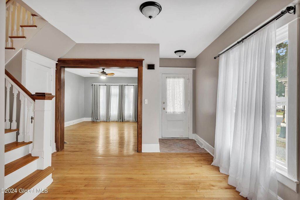 An empty living room with hardwood floors and white curtains
