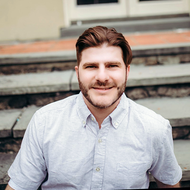 Smiling man in a light gray shirt sitting on outdoor steps
