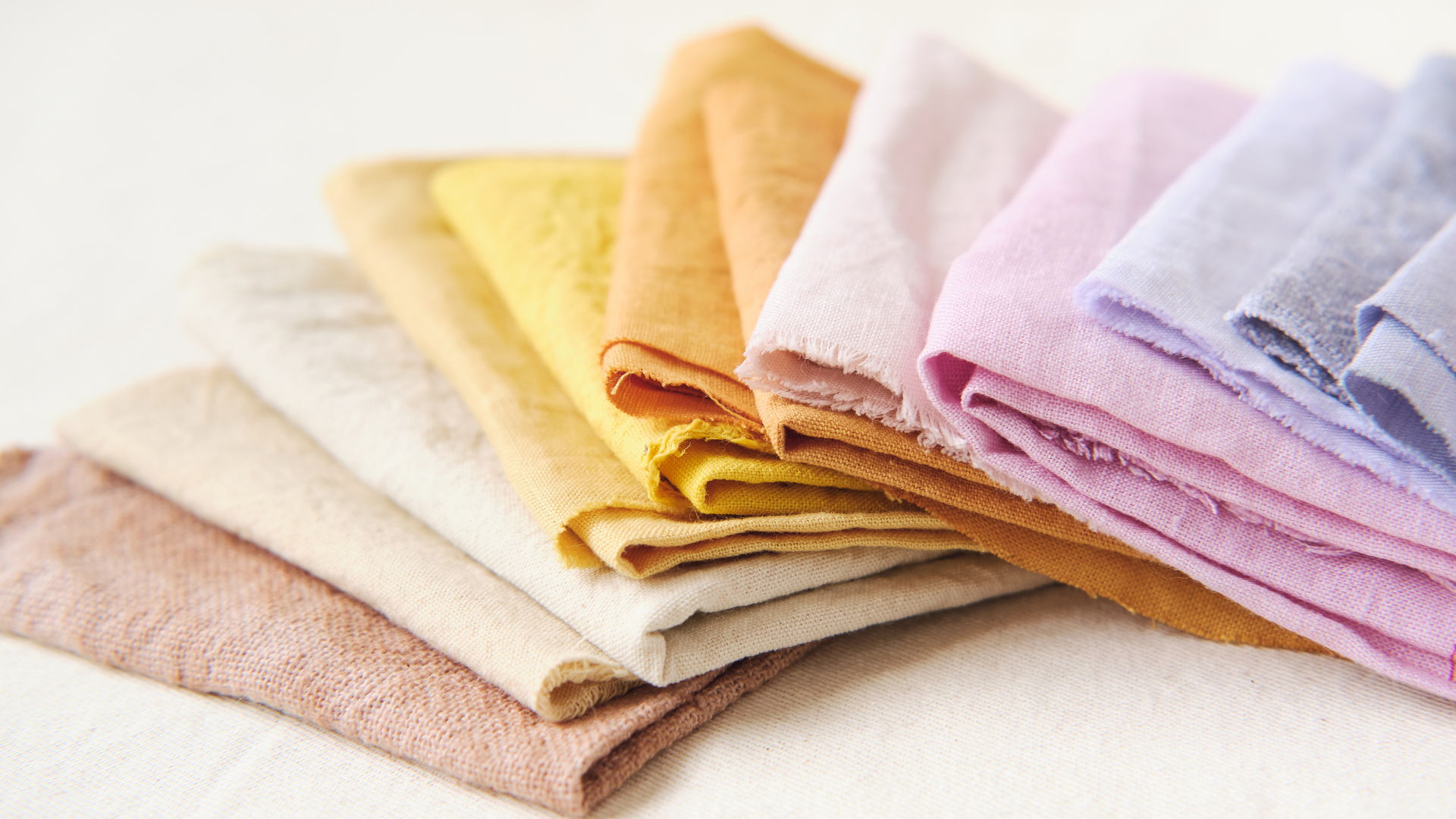 A bunch of different colored fabrics are stacked on top of each other on a table.
