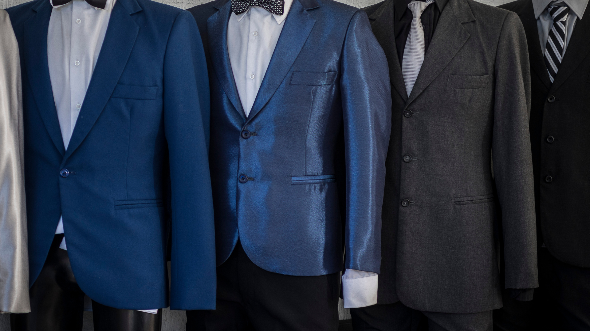 A group of men 's suits are lined up on mannequins.