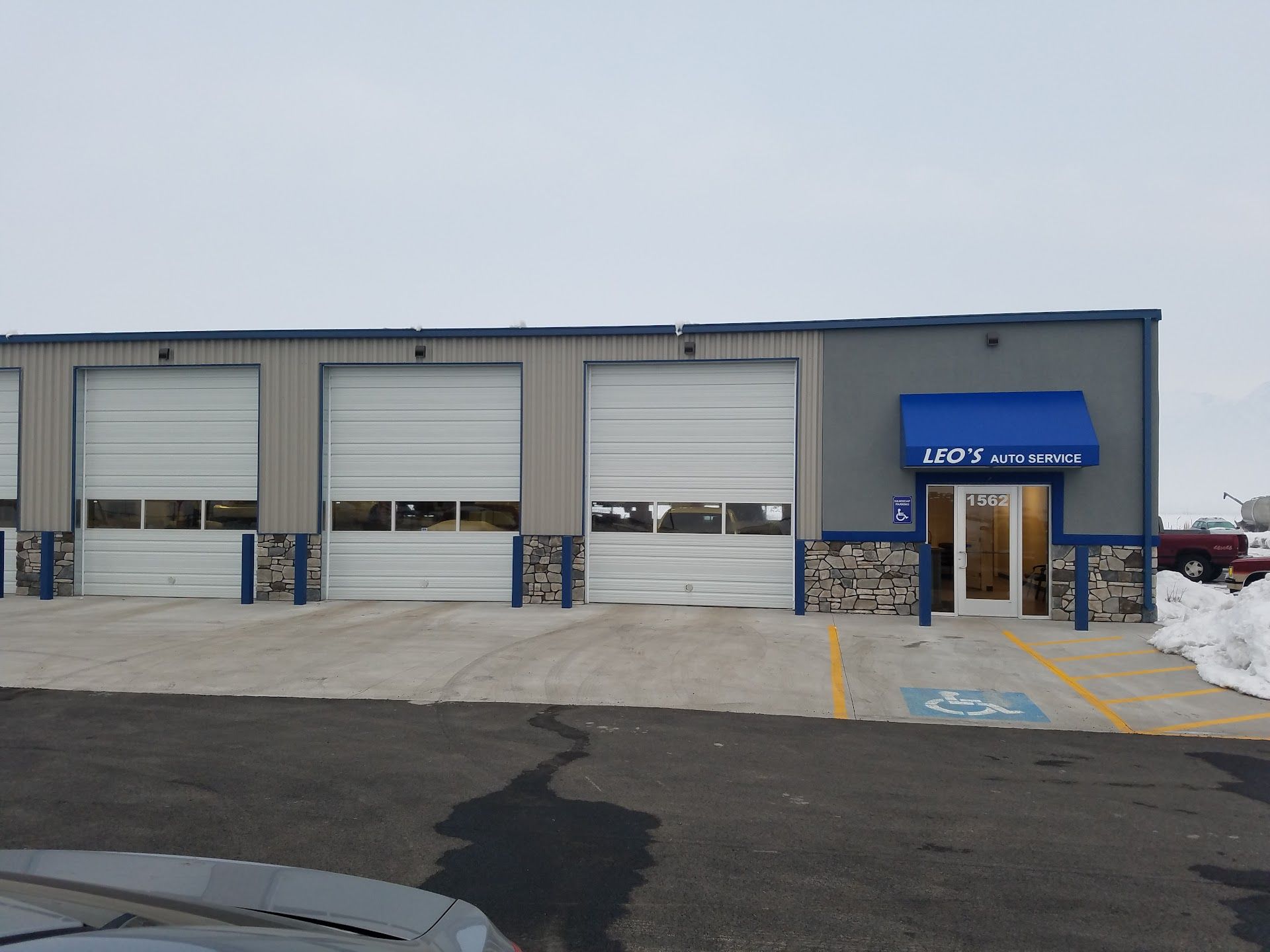Snowy parking lot outside a small industrial building with garage doors and a blue awning entrance | Leo's Auto Service
