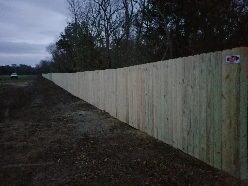 Long wooden fence along a dirt roadside at dusk, with trees in the background