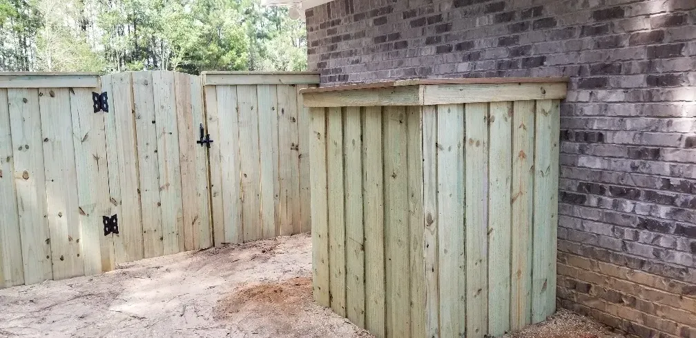 Two wooden outdoor storage enclosures beside a brick house and fence