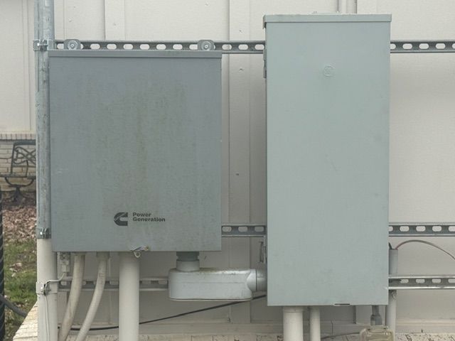 Two gray electrical utility cabinets mounted on a building exterior with connecting conduits.