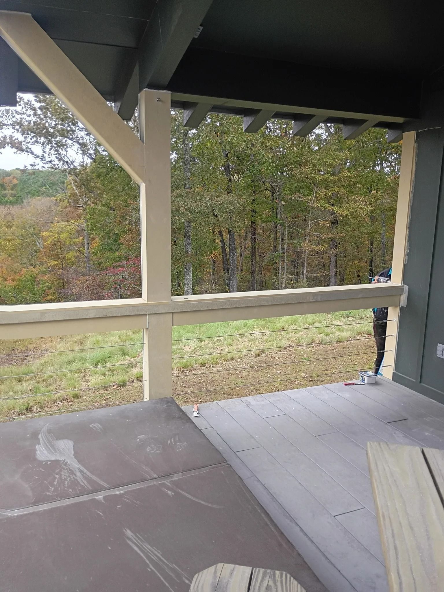 Covered porch with wooden railing and steps overlooking a wooded yard