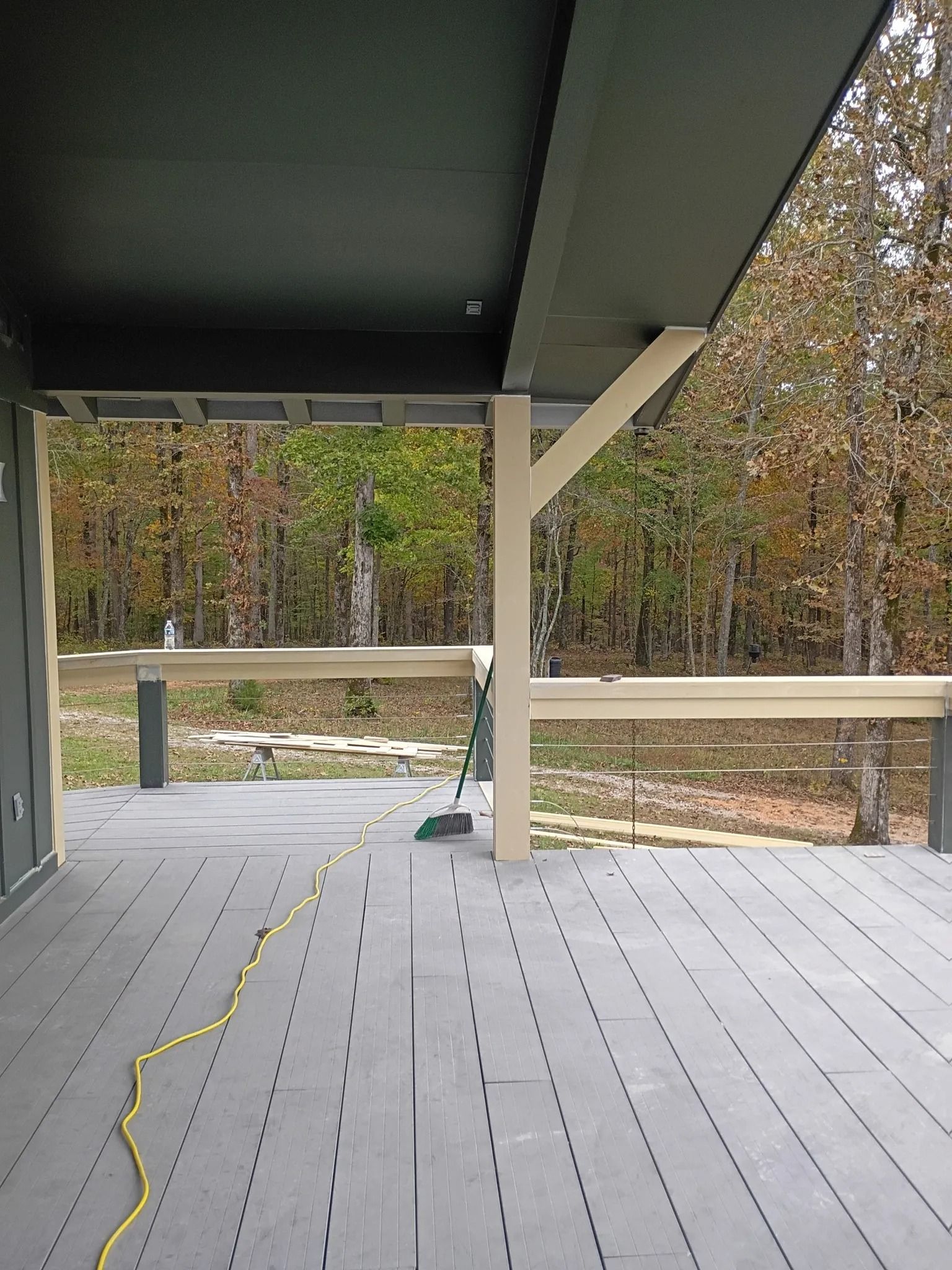 Covered wooden deck with a yellow cord, white railing, and trees beyond the porch.