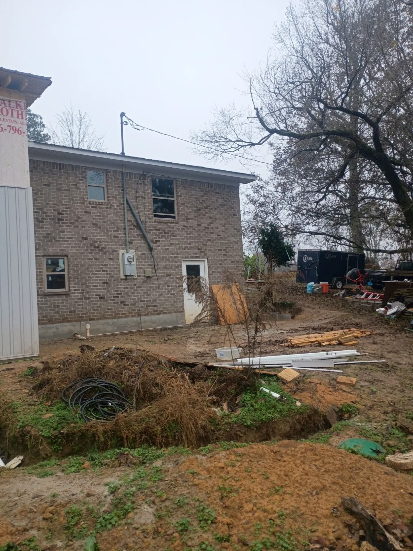 Muddy yard beside a stone house, with scattered debris and bare trees under an overcast sky.