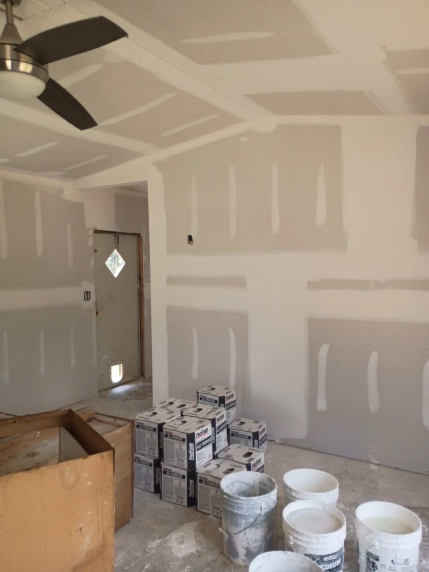 Unfinished room with drywall, paint buckets, and a ceiling fan during interior renovation