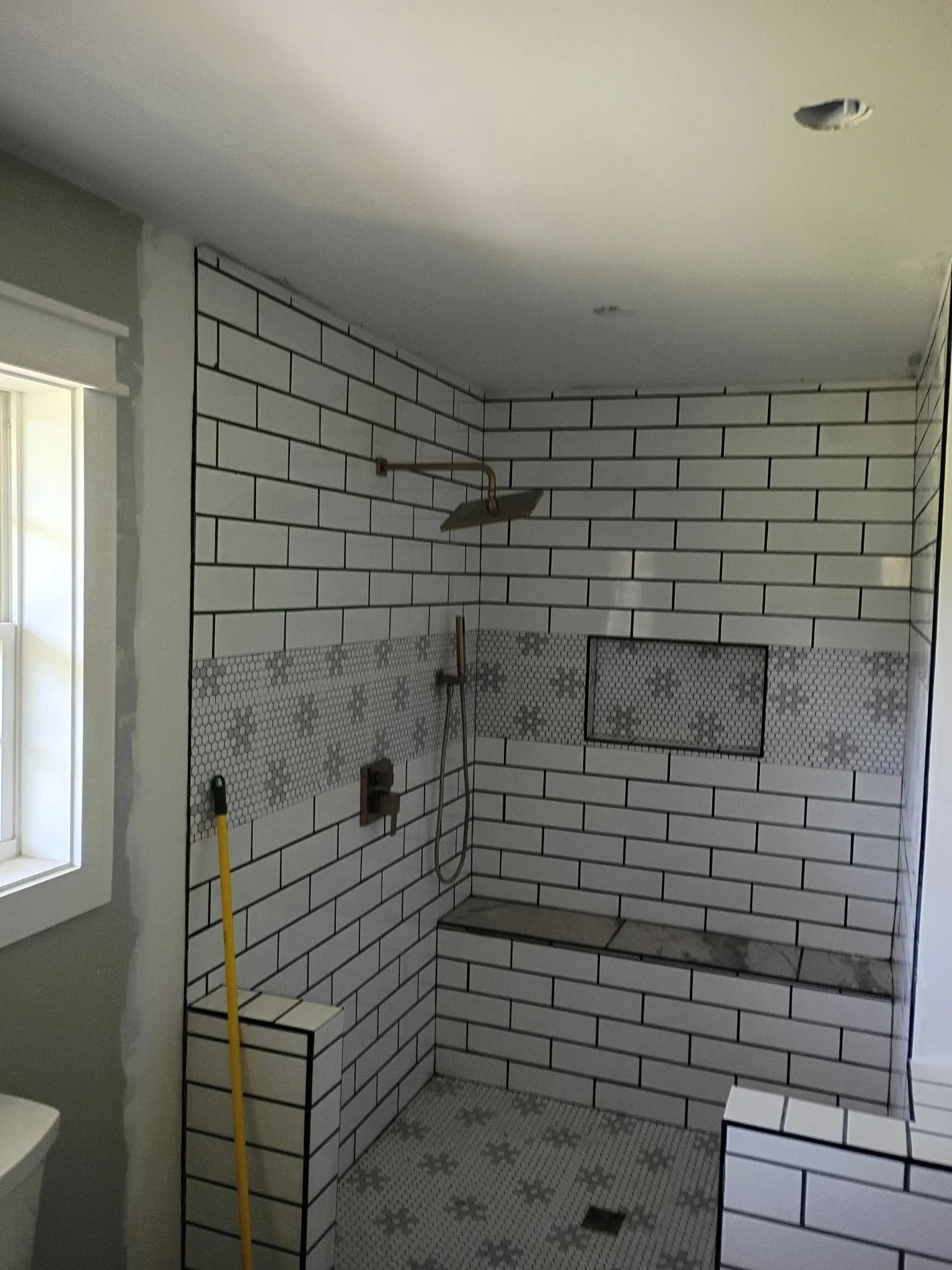 Tiled bathroom shower under construction with white subway tiles and gray mosaic floor.