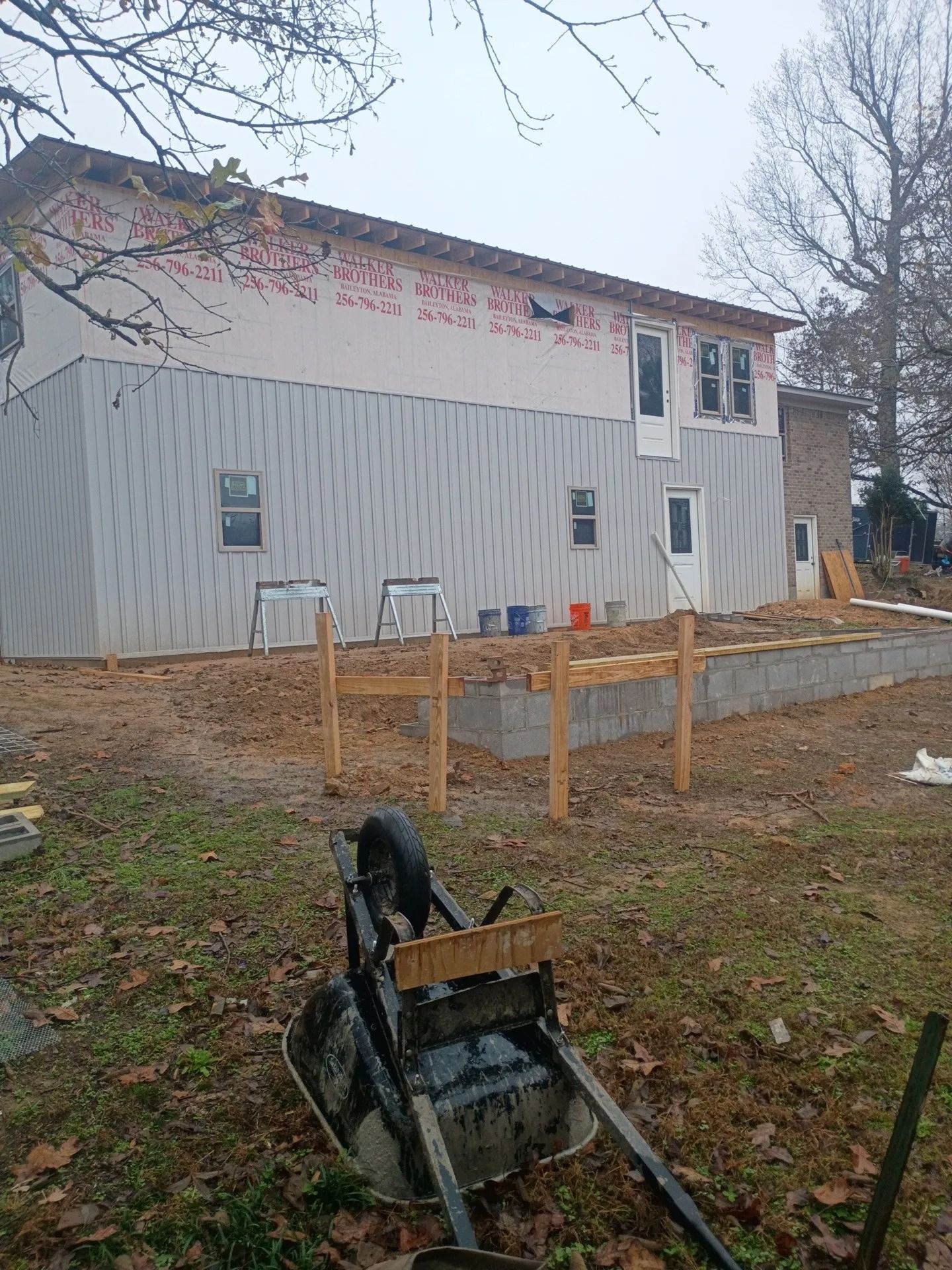 Two-story house under renovation with exposed siding, boarded windows, and construction materials in the yard