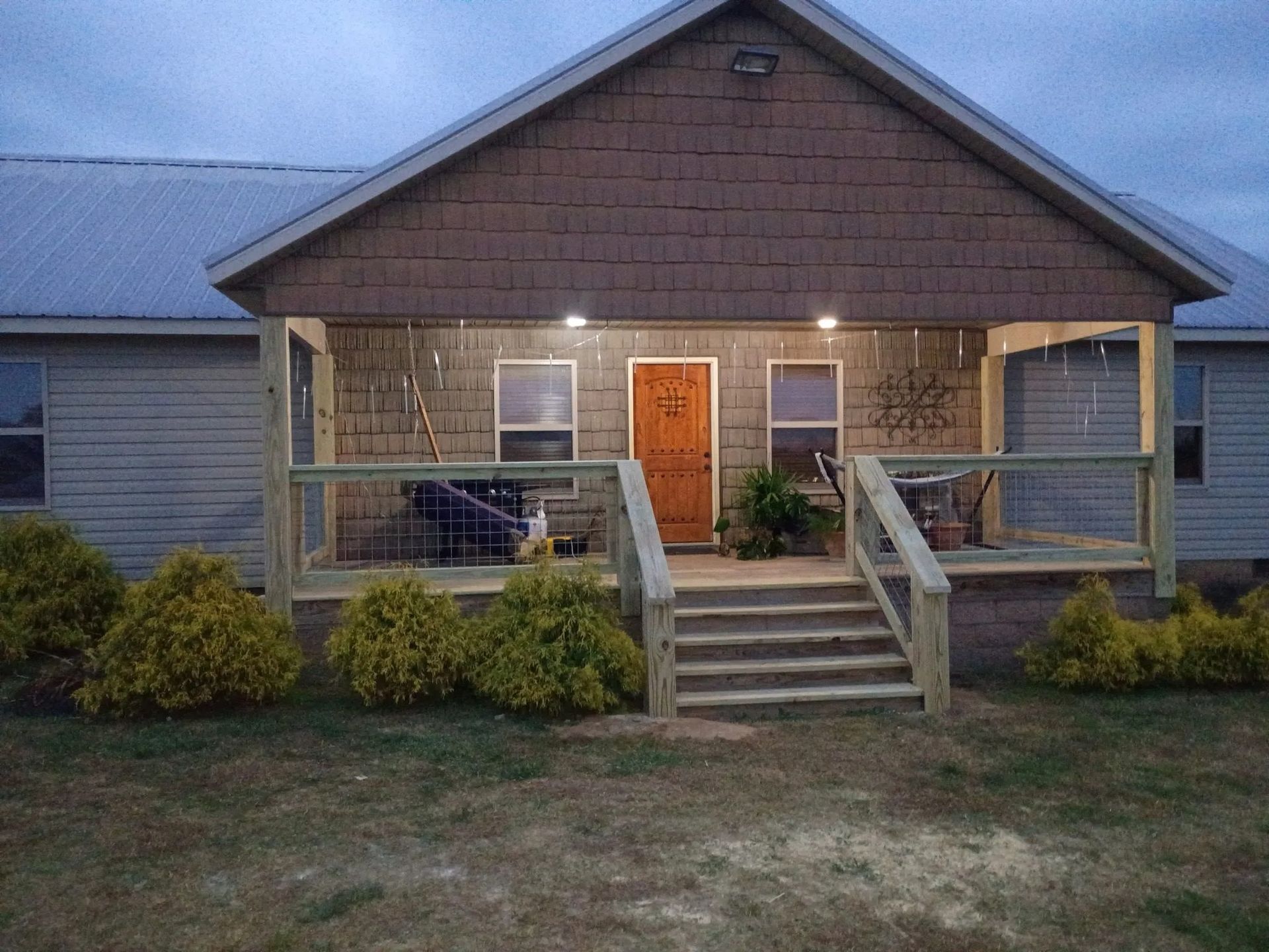 Small house with a front porch, steps, and orange front door at dusk