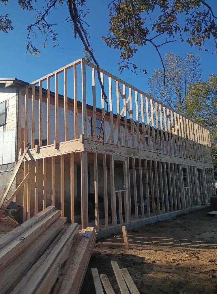 Partially framed two-story house under construction with wooden beams and a blue sky above