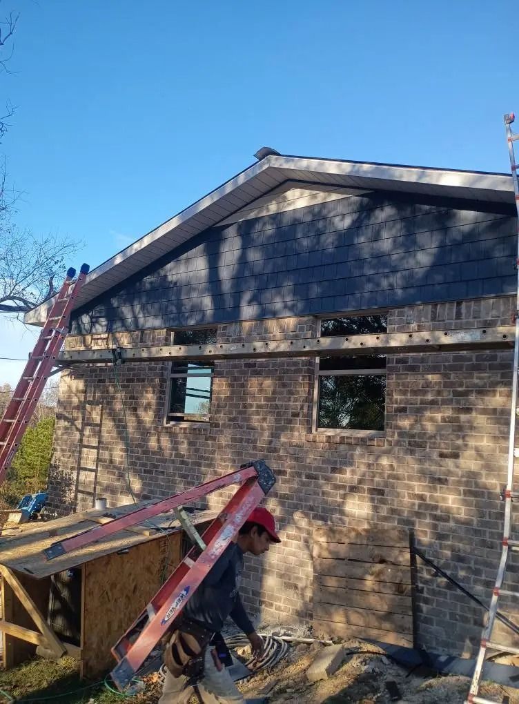 Workers repairing a brick house roof with a red ladder and scaffolding under a clear blue sky