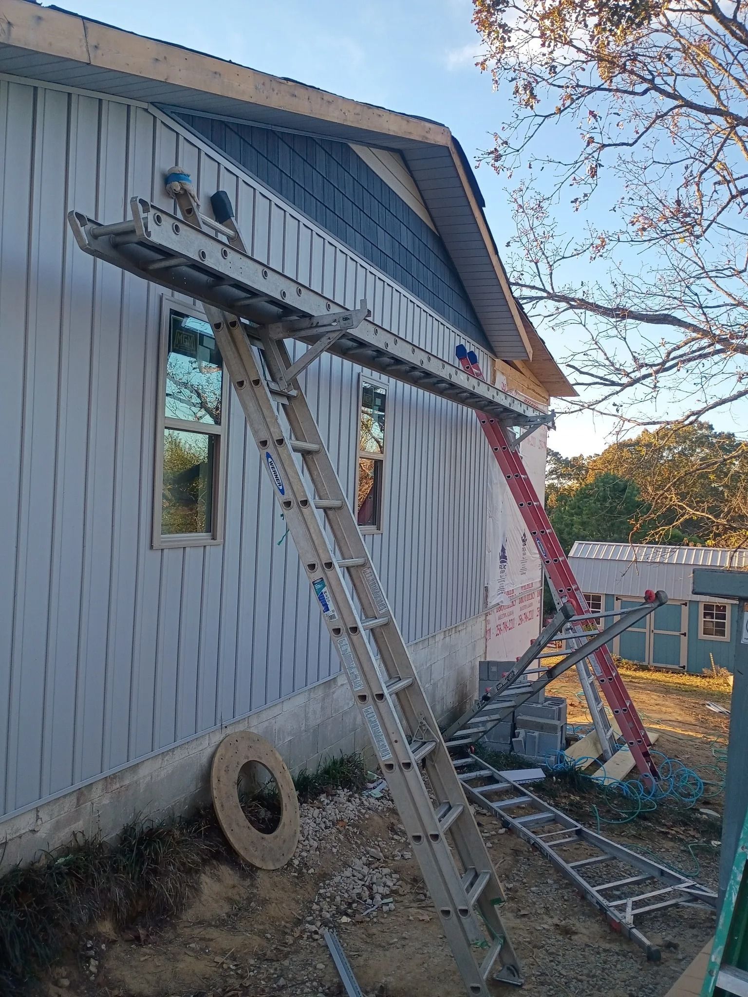 Ladders leaning against a house under repair, with construction debris and a wheelbarrow nearby.