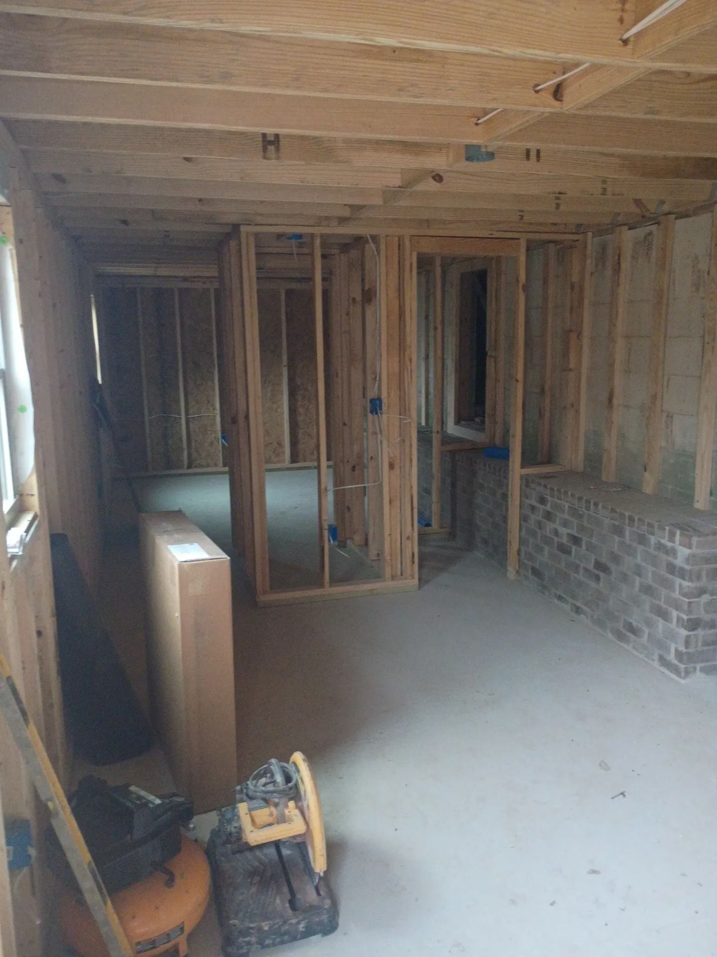 Unfinished interior framing with exposed studs, a brick wall section, and construction tools on the floor
