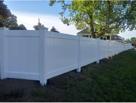 White vinyl privacy fence in a grassy yard, under a blue sky, near a house.
