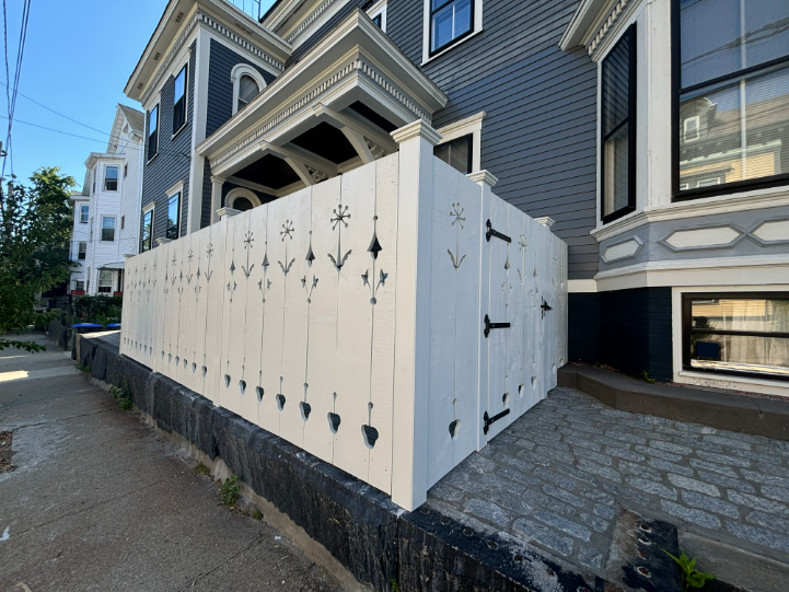 White decorative fence beside a gray building with black accents; sunny outdoor setting.