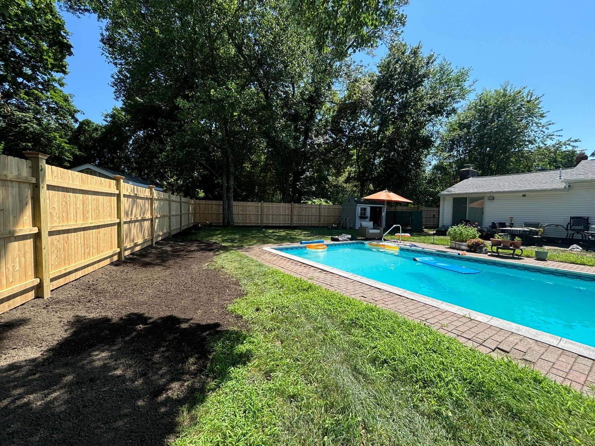 Backyard with a swimming pool, new fence, and lawn. Bright blue water, brown fence, and green grass.
