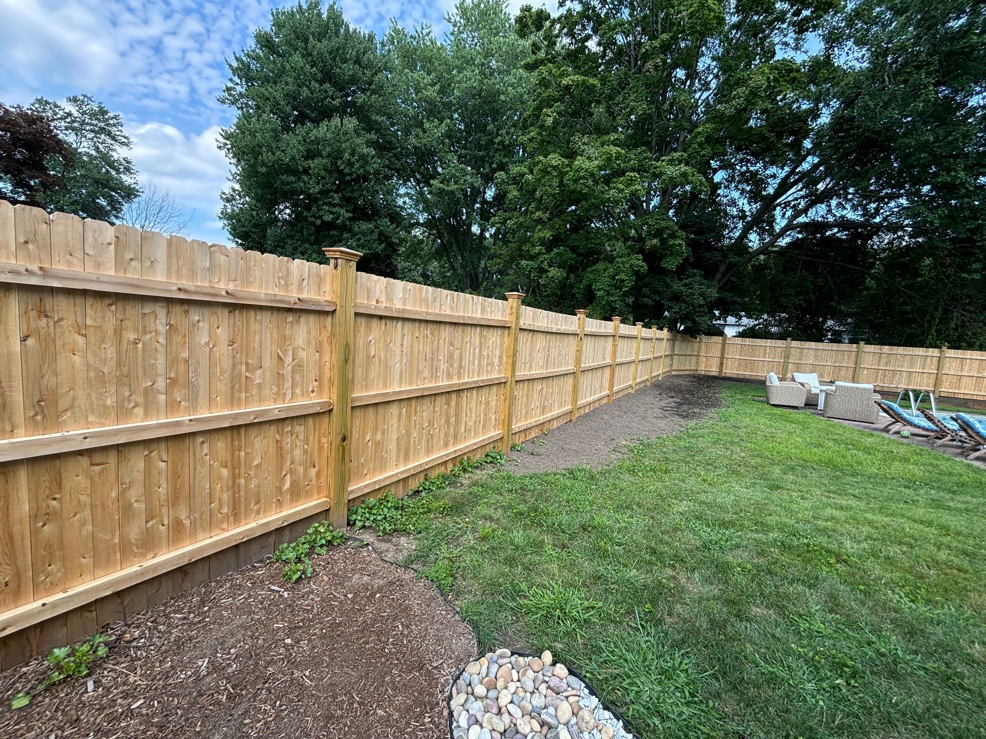 Wooden fence enclosing a grassy yard with trees and cloudy sky.