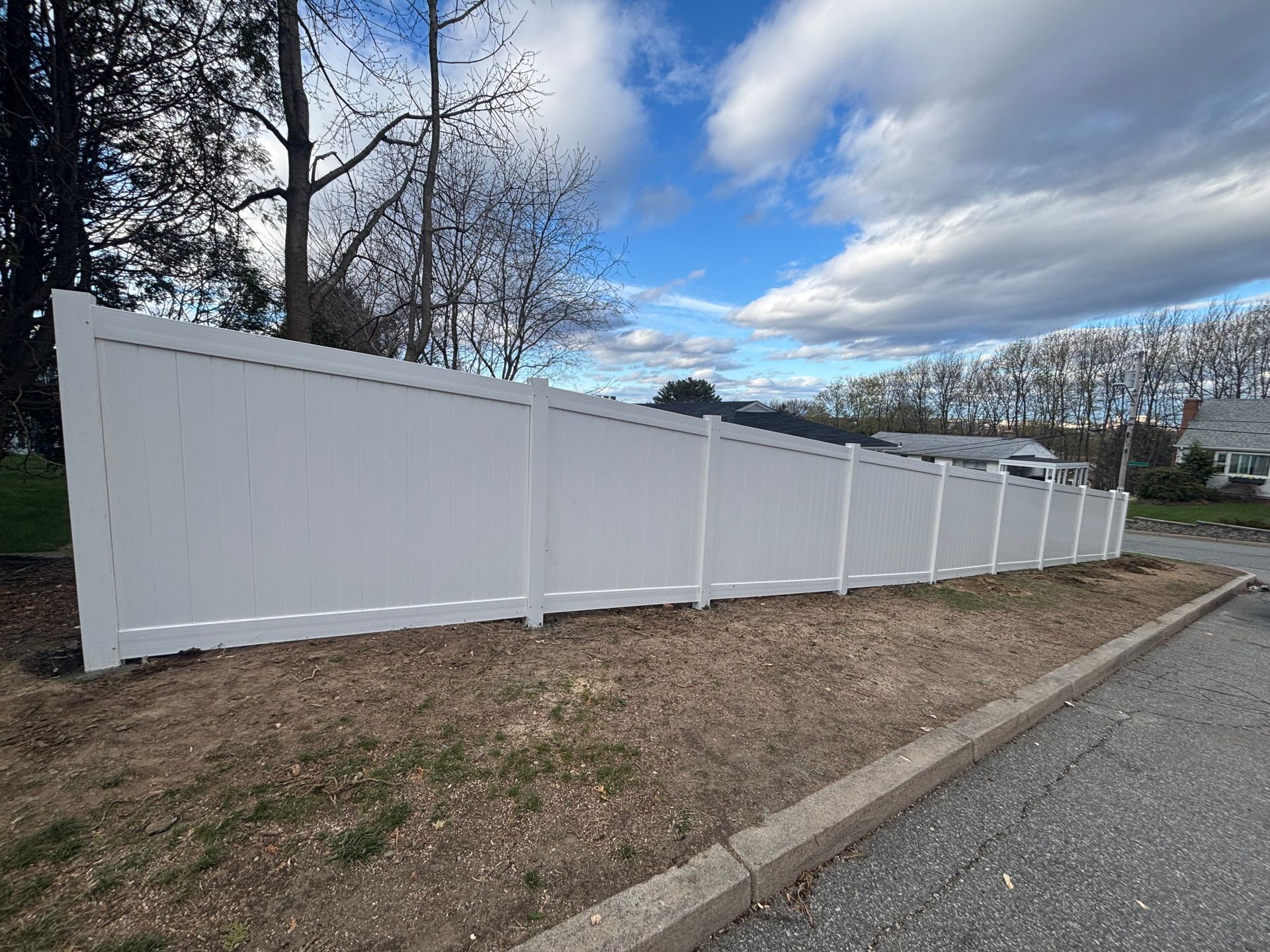 White vinyl fence along a gravel road under a cloudy sky.