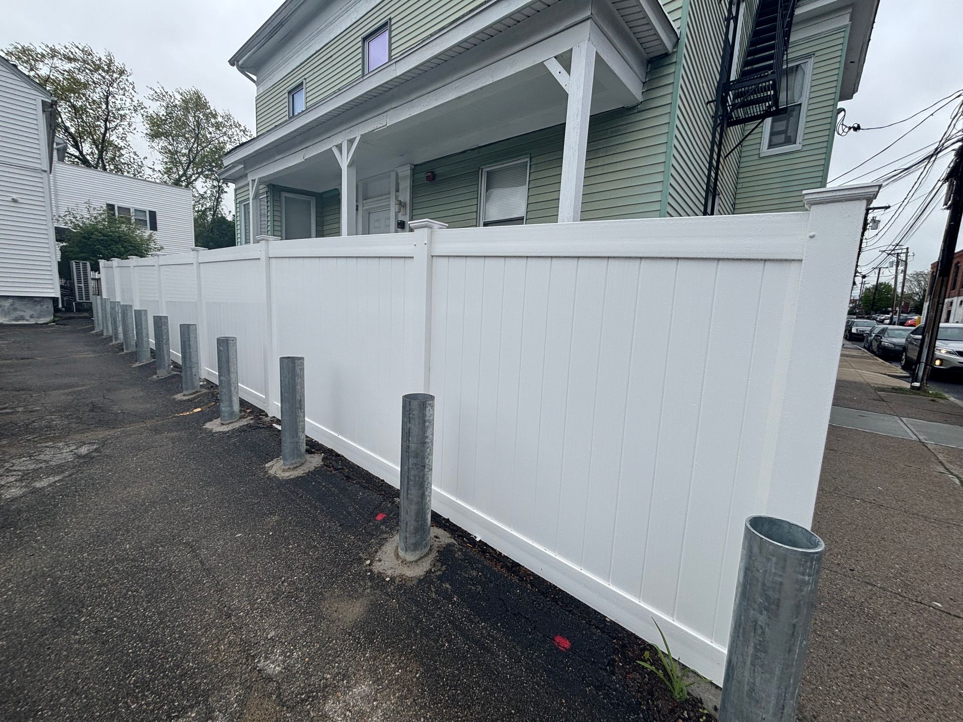 White fence with vertical metal posts lining a narrow alley next to a green building.