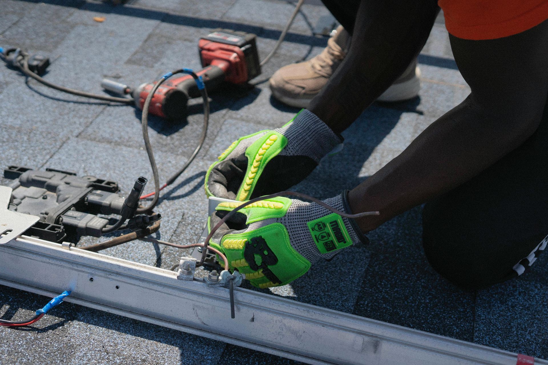 Person in safety gloves connecting wires on a rooftop solar panel, with tools nearby.