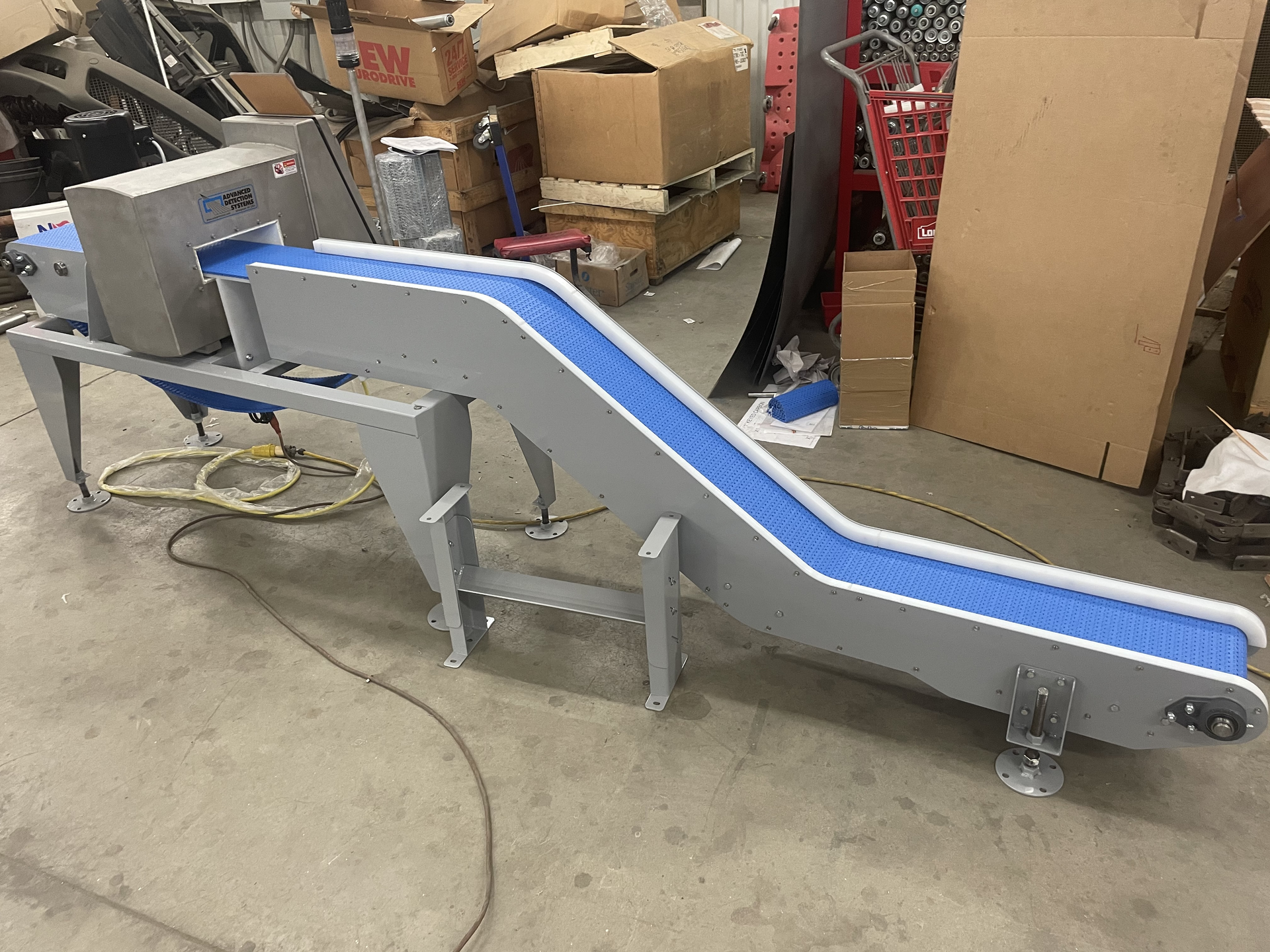 A gray industrial inclined conveyor belt with a blue surface and metal detector unit in a warehouse setting.