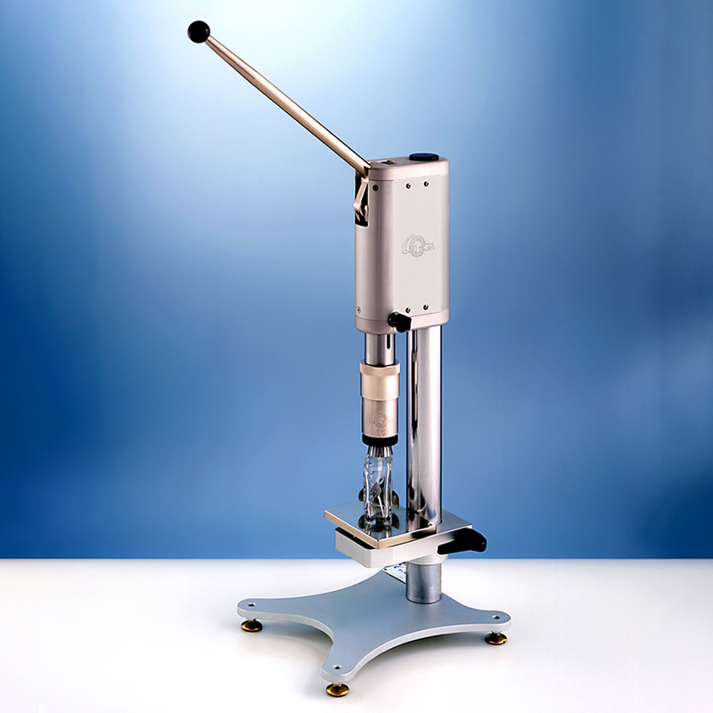 A manual, silver metal benchtop vial crimper standing on a white surface.