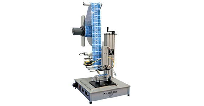 A tabletop semi-automatic label applicator machine with a roll of blue labels positioned on a silver base.