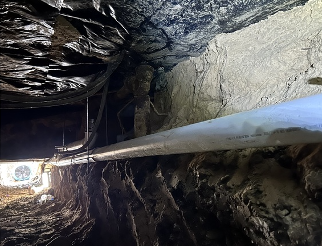 Inside a rocky tunnel, a long metal pipe runs toward a bright opening