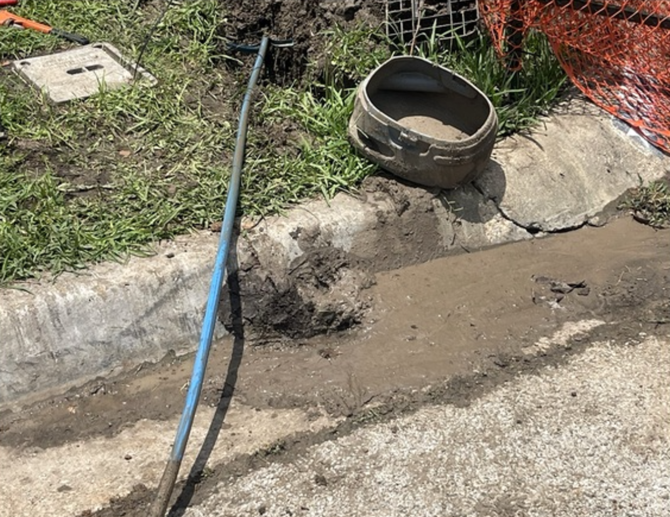 Blue hose beside a muddy roadside ditch with a concrete culvert opening and a round pipe ring