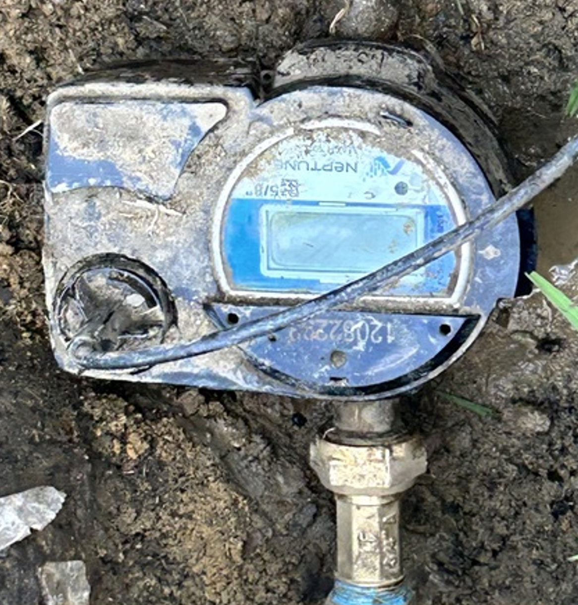 Blue water meter partly buried in dirt, with a cable across it and a pipe fitting below