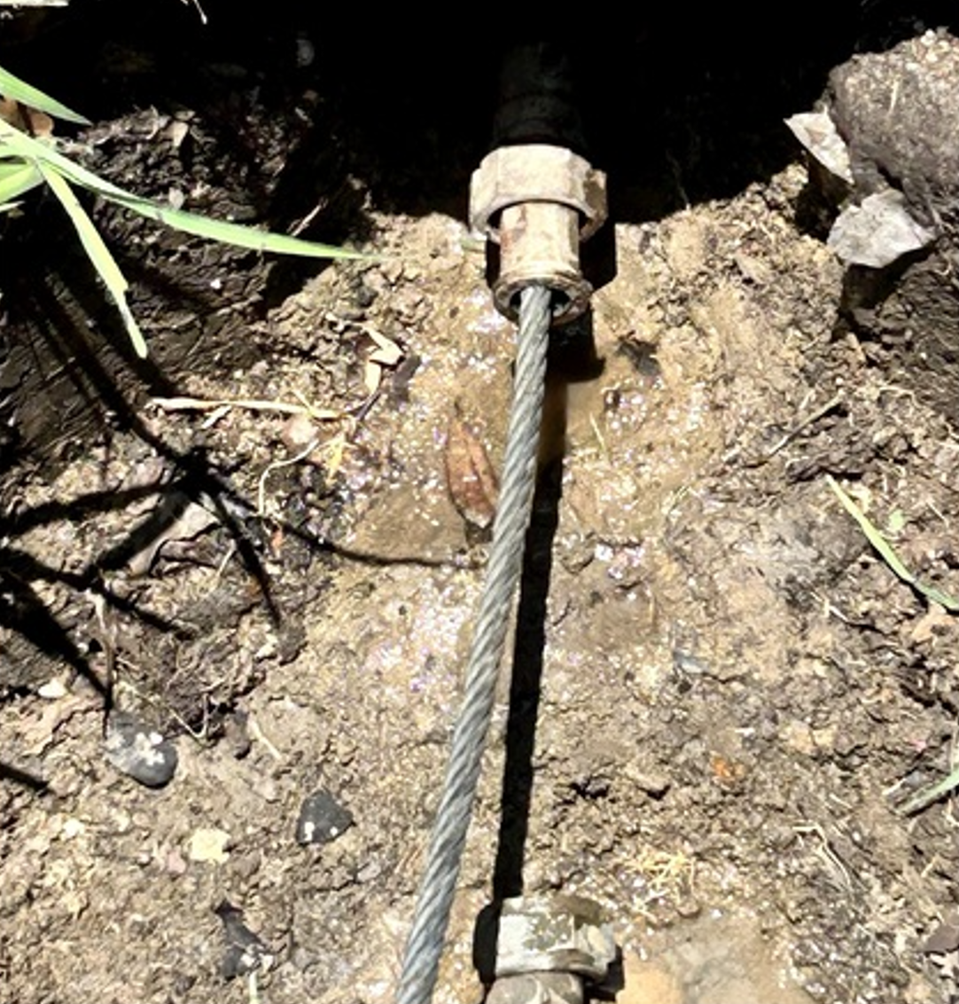 Steel cable attached to a bolt in a muddy ground close-up