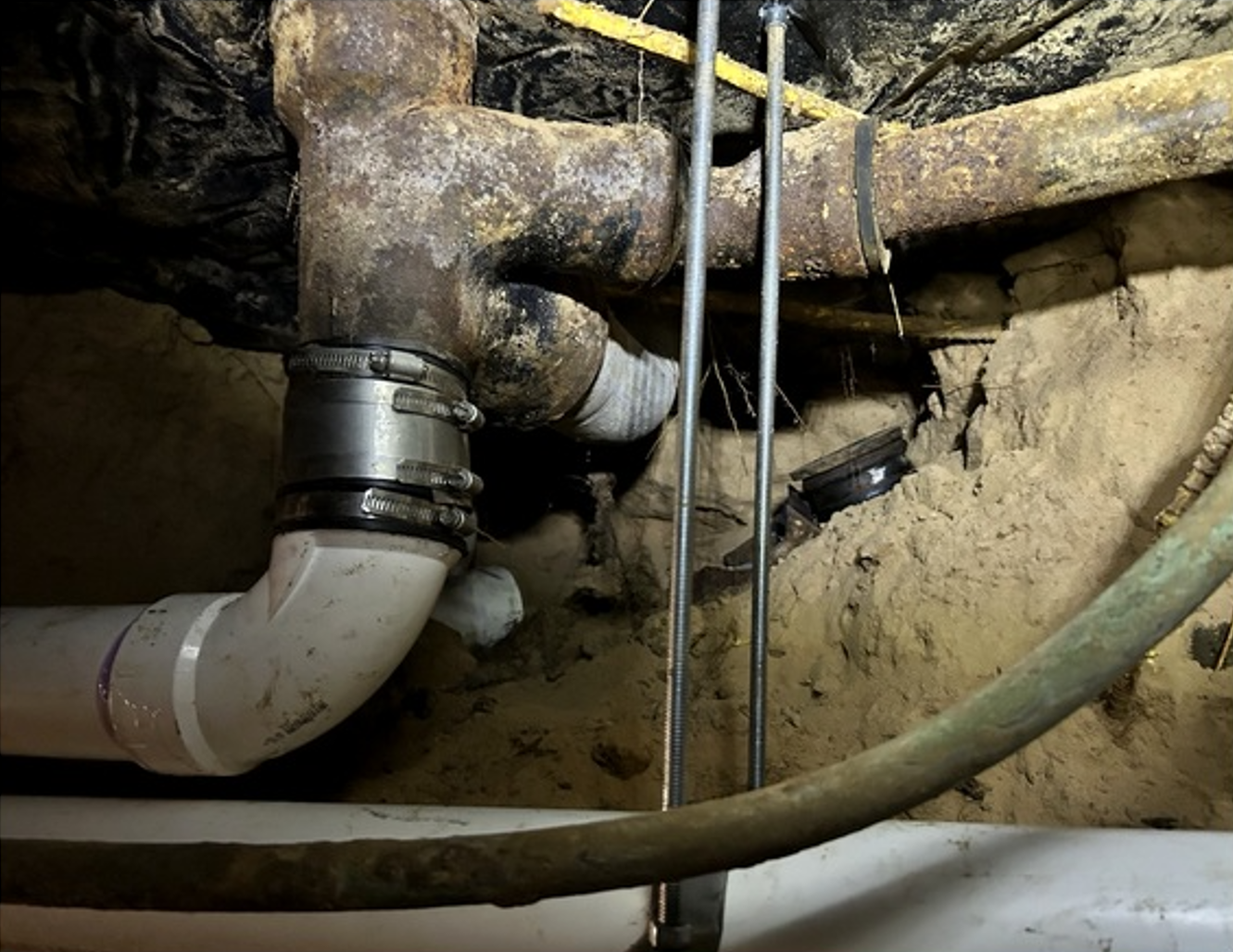 Close-up of exposed plumbing pipes and fittings in a crawlspace or basement wall cavity.