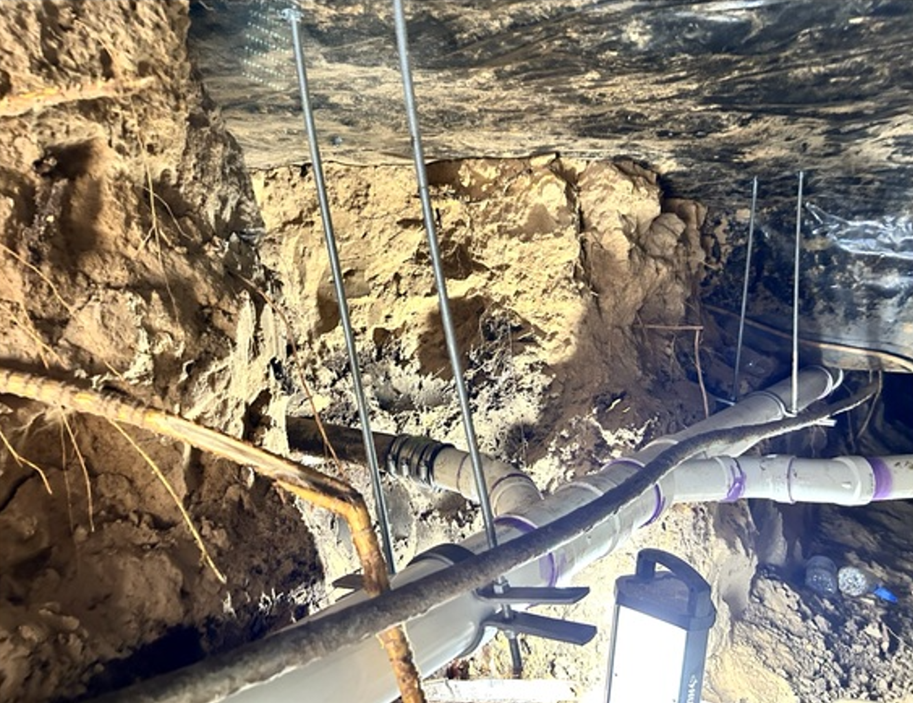 Cave wall with metal pipes and cables running through a rough, rocky excavation area