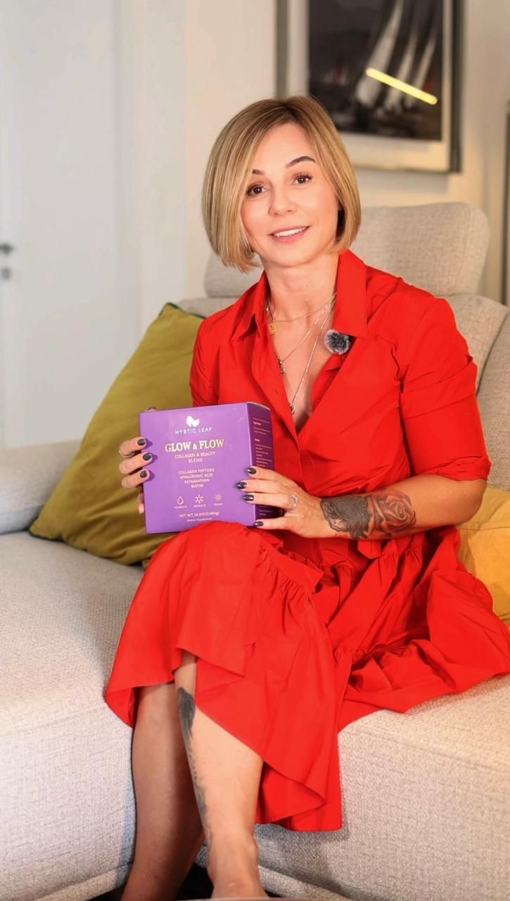 Woman in a bright red dress sits on a sofa, holding a purple book and smiling at the camera.