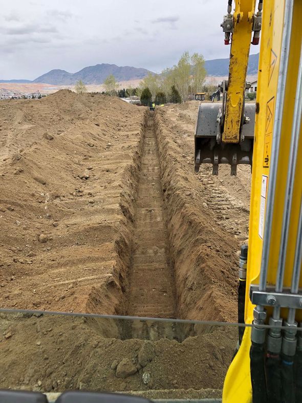 A person wearing gloves works to install corrugated drainage pipe in a gravel-filled trench.