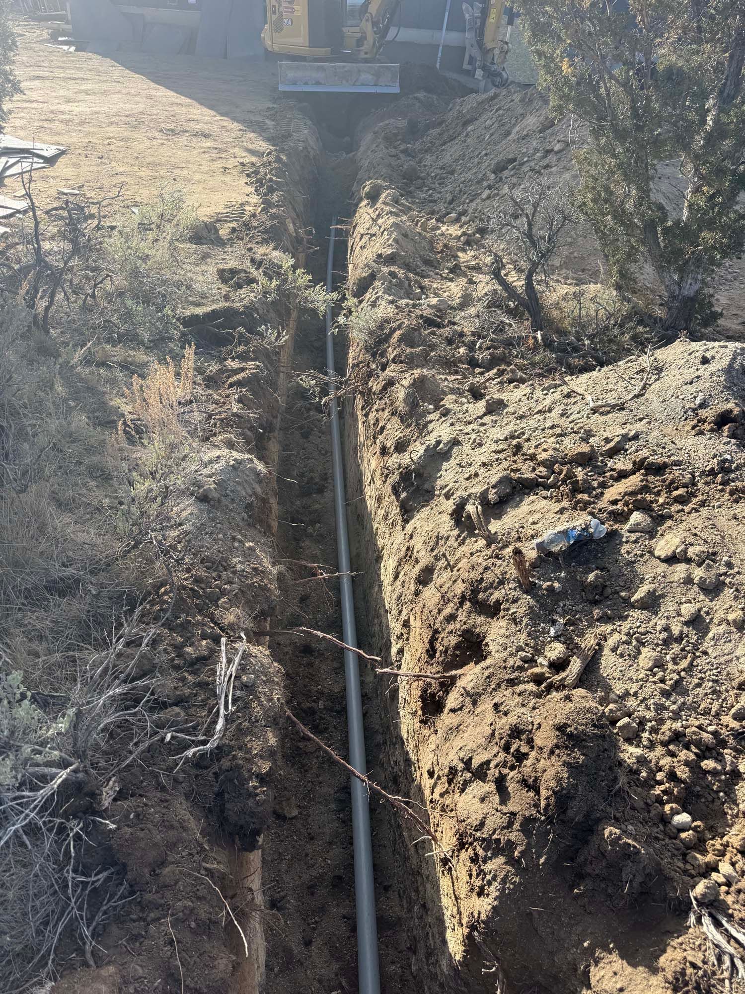 Trenched ground with a buried utility pipe and an excavator in the background on a dirt site